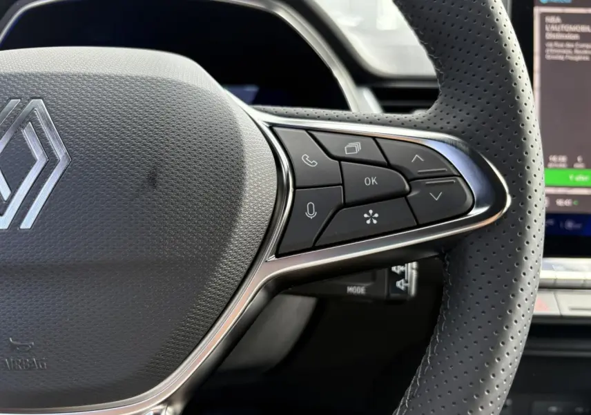 Gros plan sur le volant en cuir perforé de la Renault SYMBIOZ 2025 avec commandes multifonctions et logo central argenté.
