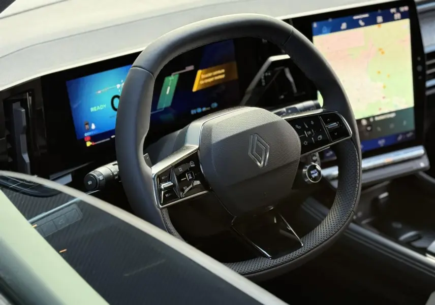 Volant Renault en cuir noir avec commandes intégrées, tableau de bord numérique et écran tactile central visible de face.