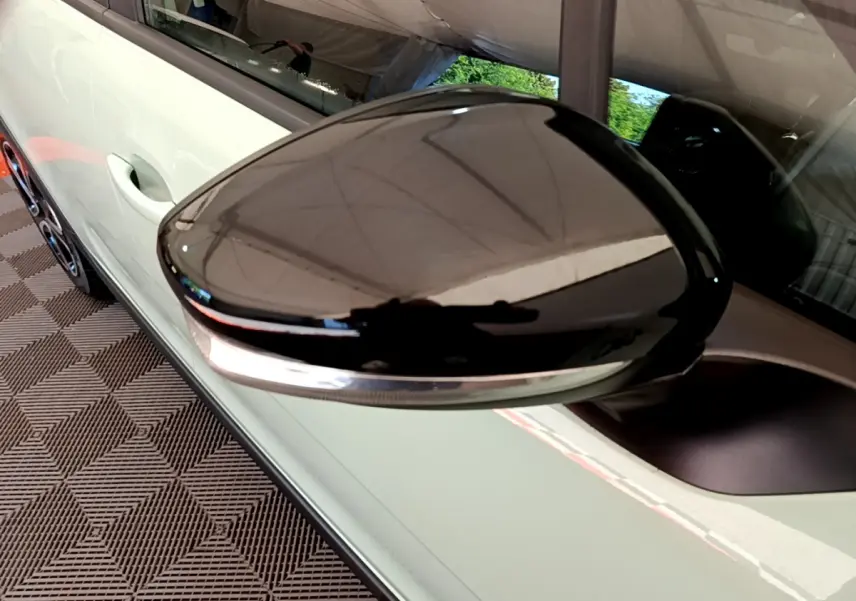 Gros plan sur le rétroviseur droit noir brillant d'une Citroën C3 vert clair, avec poignée de porte visible en arrière-plan.
