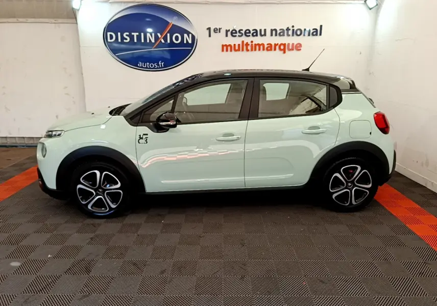 Profil côté gauche d'une Citroën C3 PureTech 82 S&S BVM Graphic vert clair avec toit noir et jantes stylisées en intérieur showroom.