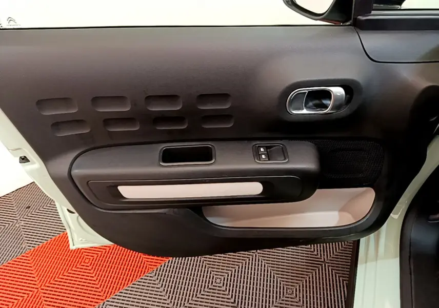 Intérieur côté gauche de la porte d'une Citroën C3 vert clair, avec poignée argentée et commandes de vitres.