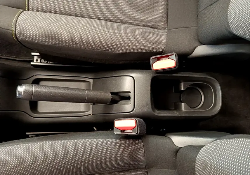 Vue plongeante sur la console centrale noire avec frein à main et ceintures rouges de la Citroën C3 verte.