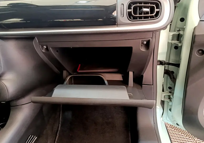 Vue rapprochée de la boîte à gants ouverte côté passager d'une Citroën C3 vert clair, tableau de bord noir brillant.