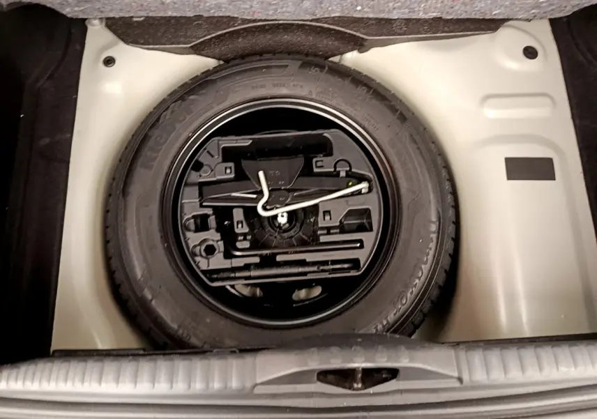 Vue plongeante sur la roue de secours et l'outillage dans le coffre d'une Citroën C3 vert 2019.