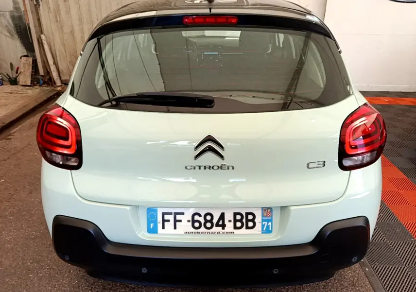 Vue arrière d'une Citroën C3 vert clair avec toit noir et feux arrière rouges dans un garage.