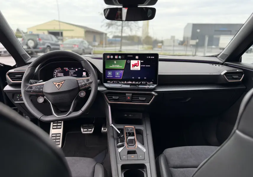 Vue intérieure avant du CUPRA Formentor 1.5 eHybrid 2025, tableau de bord noir avec écran tactile central et volant multifonction.