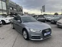 Audi A6 Avant 2.0 TDI S-Line gris métal vue 3/4 avant sur un parking extérieur avec plusieurs voitures autour.