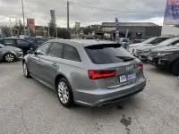 Audi A6 Avant 2.0 TDI S-Line gris métal vue 3/4 arrière droit sur parking avec plusieurs voitures autour.