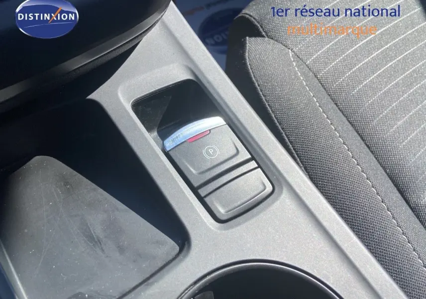 Gros plan sur la console centrale avec frein à main électrique et tissu gris noir du siège d’une Renault Arkana noire.