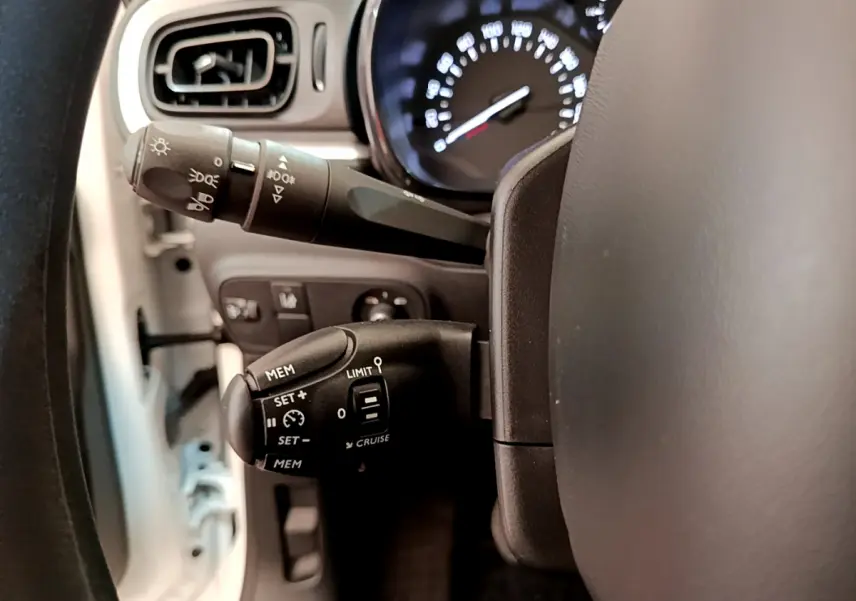 Gros plan sur la commande de régulateur de vitesse à gauche du volant d'une Citroën C3 blanche de 2019.