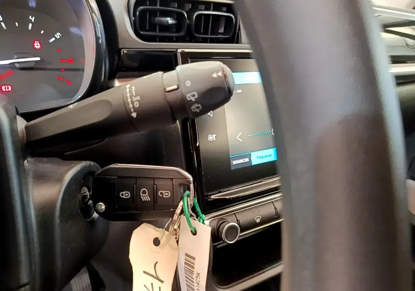 Vue rapprochée du tableau de bord et de la clé insérée dans le contact d'une Citroën C3 blanche, écran tactile visible.