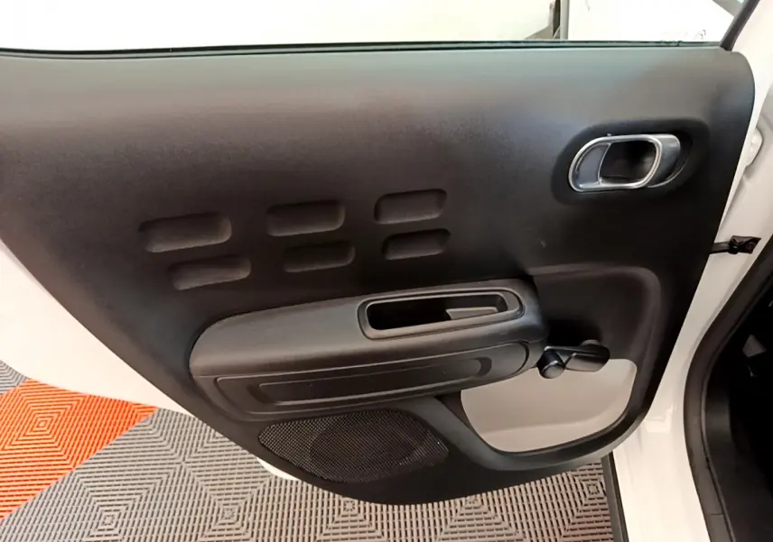 Vue rapprochée de la porte arrière droite blanche de la Citroën C3 2019 avec poignée intérieure noire et manivelle de vitre.