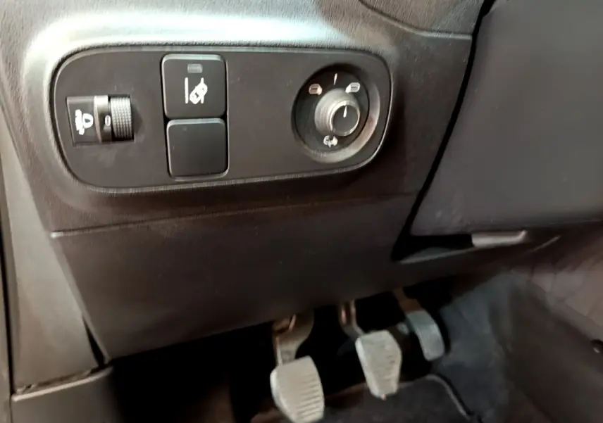 Vue rapprochée côté gauche du poste de conduite de la Citroën C3 blanche, avec commandes et pédales manuelles visibles.