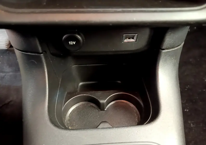 Gros plan sur la console centrale noire de la Citroën C3, montrant prise 12V et port USB au-dessus des porte-gobelets.