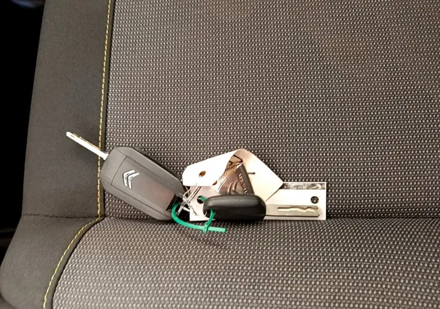 Clé de voiture Citroën posée sur un siège tissu gris foncé avec surpiqûres jaunes visibles.
