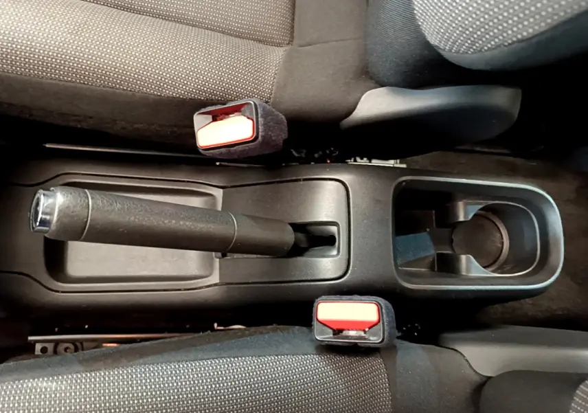 Vue plongeante sur la console centrale noire de la Citroën C3 avec frein à main manuel et ceintures de sécurité rouges.