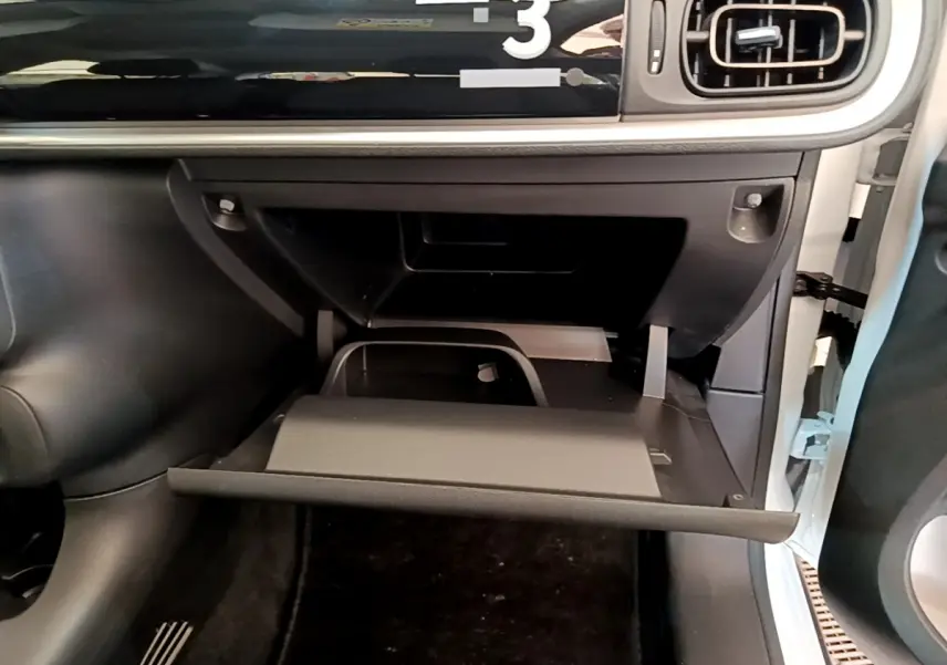 Gros plan sur la boîte à gants ouverte côté passager d'une Citroën C3 blanche, intérieur noir et beige.