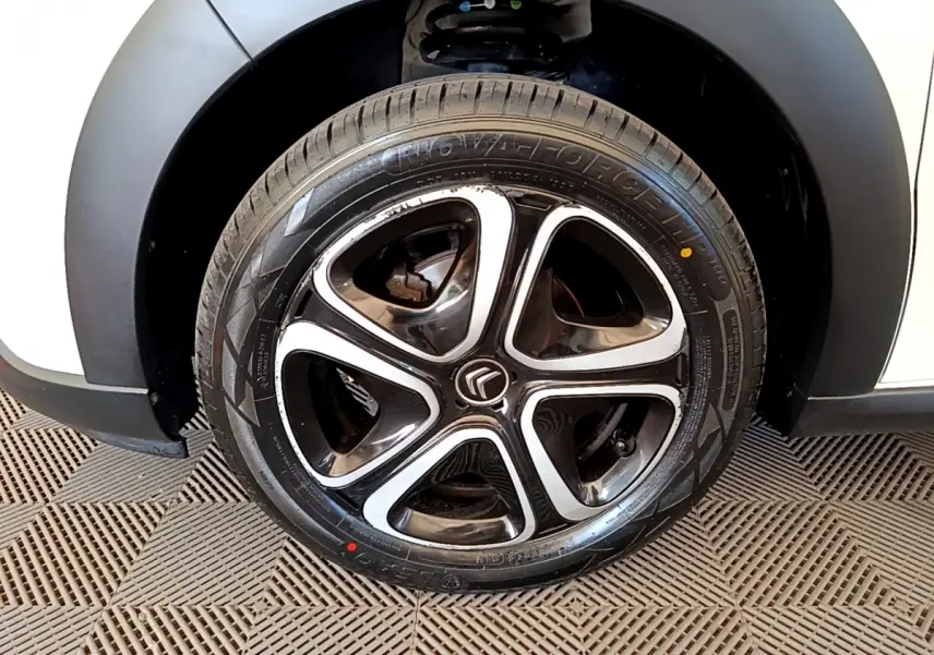 Gros plan sur la roue arrière droite d'une Citroën C3 blanche avec passage de roue noir mat et jante alliage.