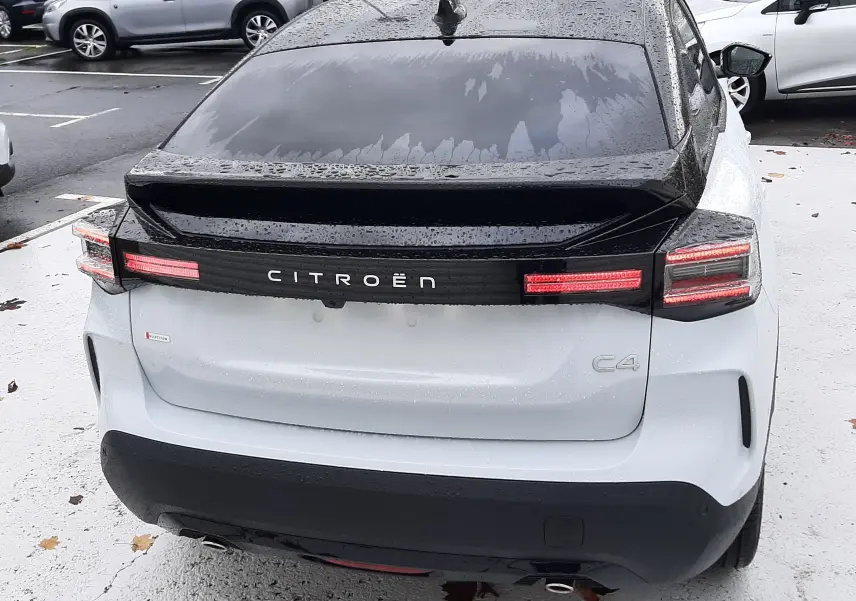 Vue arrière d'une Citroën C4 hybride blanche avec toit noir, feux arrière allumés et logo bien visible.