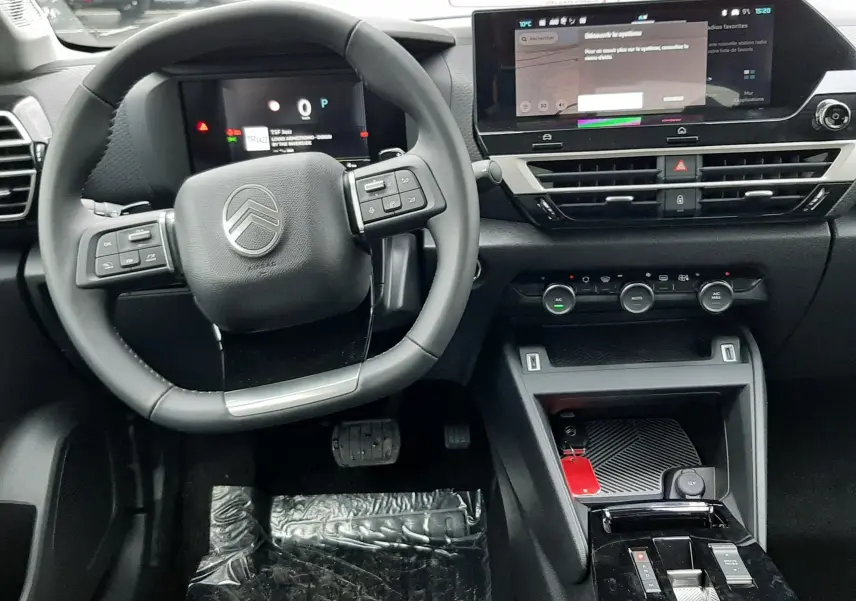 Vue intérieure du poste de conduite de la Citroën C4 hybride 2025 avec volant multifonction et écran tactile central.