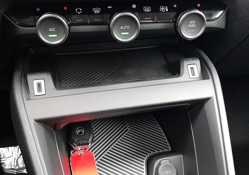 Gros plan sur la console centrale de la Citroën C4 hybride 2025, avec commandes climatisation et clé de voiture.