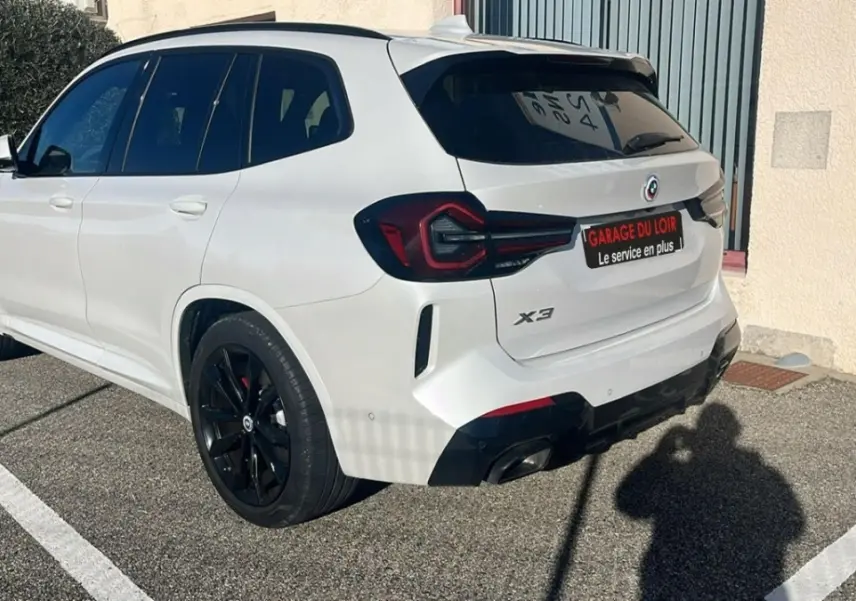 BMW X3 blanc vue 3/4 arrière droit, jantes noires et feux arrière LED distinctifs visibles.