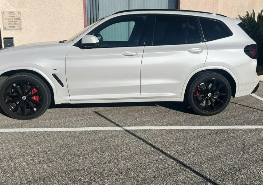 BMW X3 xDrive30d blanc vue de profil côté gauche avec jantes noires et étriers de frein rouges visibles.
