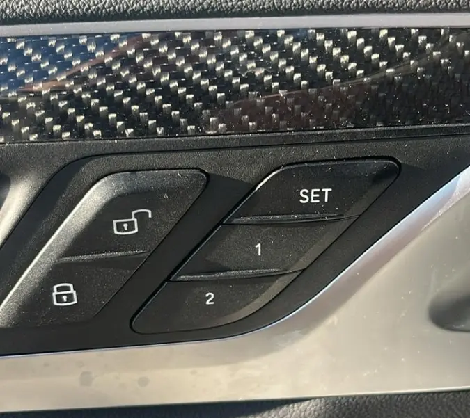 Détail intérieur côté gauche de la porte BMW X3 blanc, boutons de verrouillage et mémoire sièges avec finition carbone.