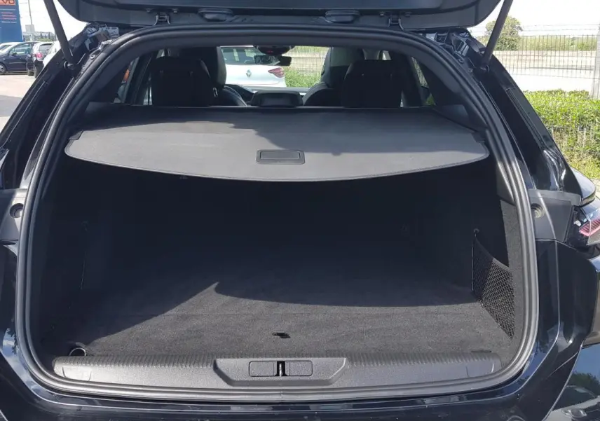 Vue arrière ouverte du coffre noir du Peugeot 308 SW PHEV 225 e-EAT8 GT avec cache-bagages et filet latéral.