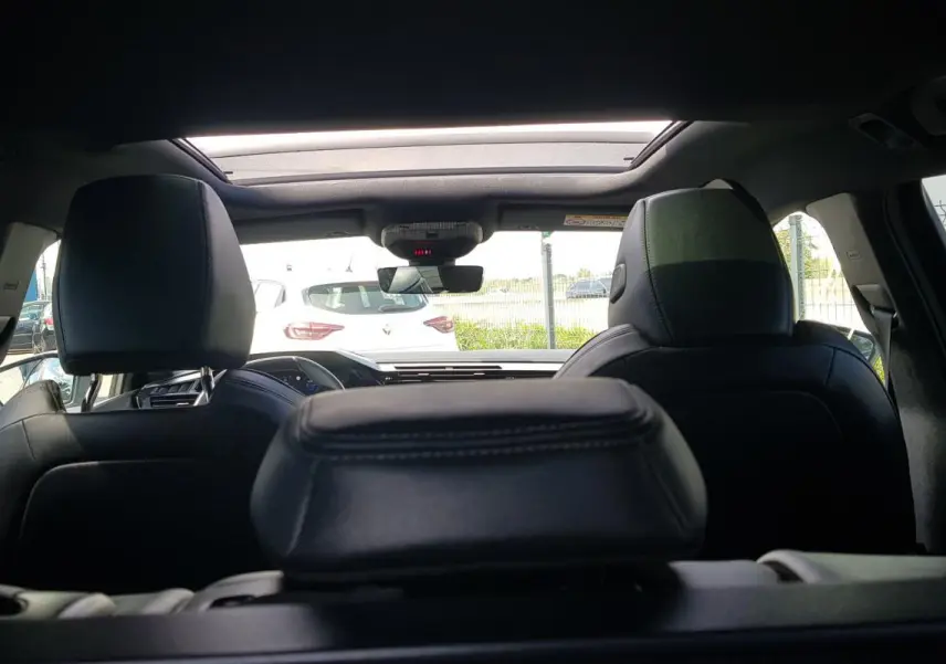 Vue intérieure arrière de la Peugeot 308 SW PHEV 225 e-EAT8 GT noire, avec toit ouvrant électrique et sièges en cuir noir.