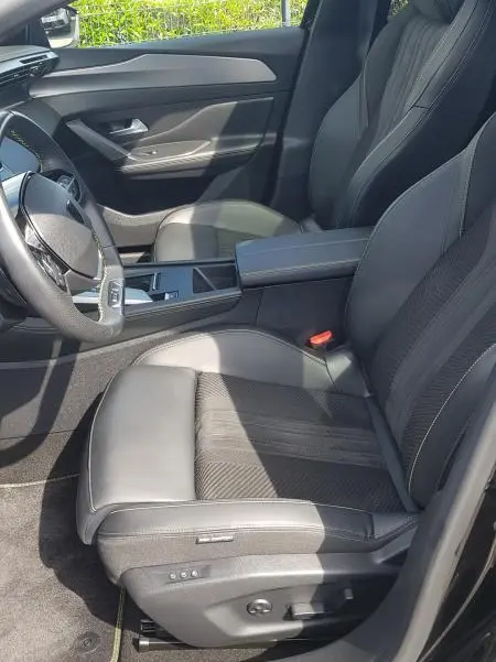 Intérieur côté conducteur de la Peugeot 308 SW PHEV 225 e-EAT8 GT 2023, sièges cuir noirs et accoudoir central visible.