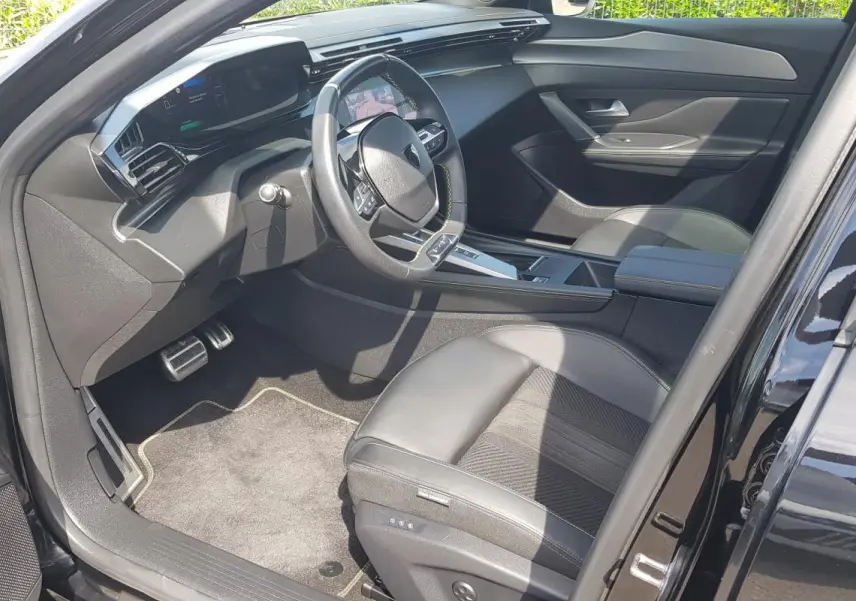 Intérieur avant droit de la Peugeot 308 SW PHEV 225 GT 2023 noir, volant cuir et cockpit numérique visible.