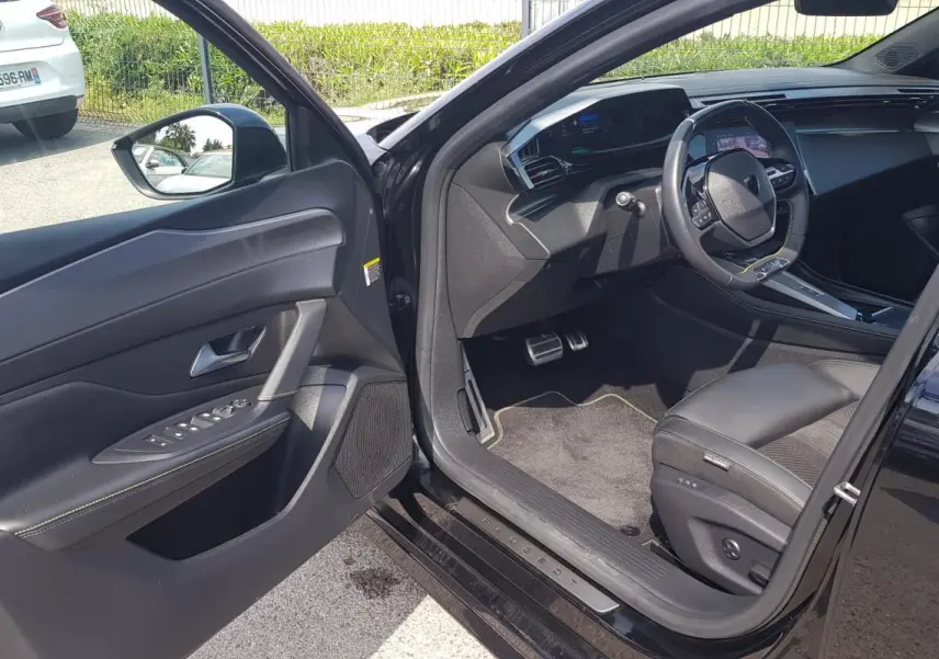 Intérieur côté conducteur de la Peugeot 308 SW PHEV noire 2023, montrant siège, volant cuir et tableau de bord numérique.