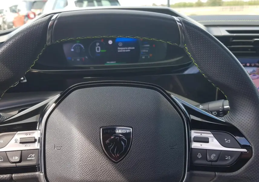 Vue rapprochée du volant cuir noir perforé de la Peugeot 308 SW PHEV 225 e-EAT8 GT avec tableau de bord numérique.