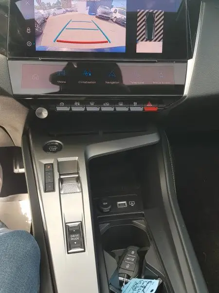 Vue intérieure centrée sur la console centrale et l'écran tactile affichant la caméra de recul du Peugeot 308 SW noir PHEV 2023.