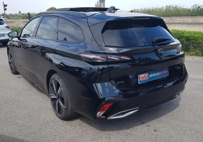 Peugeot 308 SW PHEV noir vue 3/4 arrière droit, avec jantes alliage 18 pouces et barres de toit visibles.