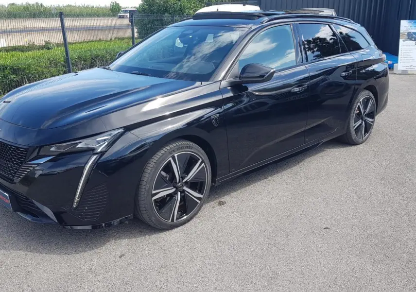 Peugeot 308 SW PHEV noir en 3/4 avant droit, avec jantes alliage 18 pouces et barres de toit visibles.