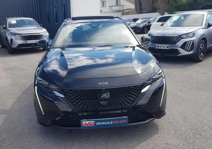 Peugeot 308 SW PHEV noir vue de face, avec calandre noire et feux LED verticaux allumés.