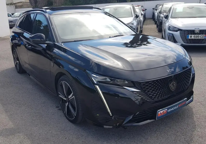 Peugeot 308 SW PHEV noir vue 3/4 avant droit, avec jantes alliage 18 pouces et barres de toit visibles.