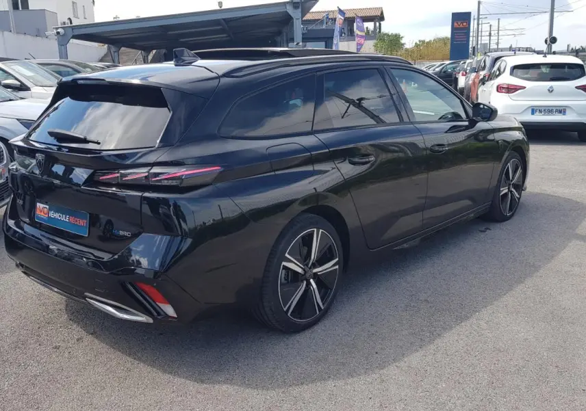 Peugeot 308 SW PHEV noir en 3/4 arrière droit, avec jantes alliage 18 pouces et barres de toit visibles.