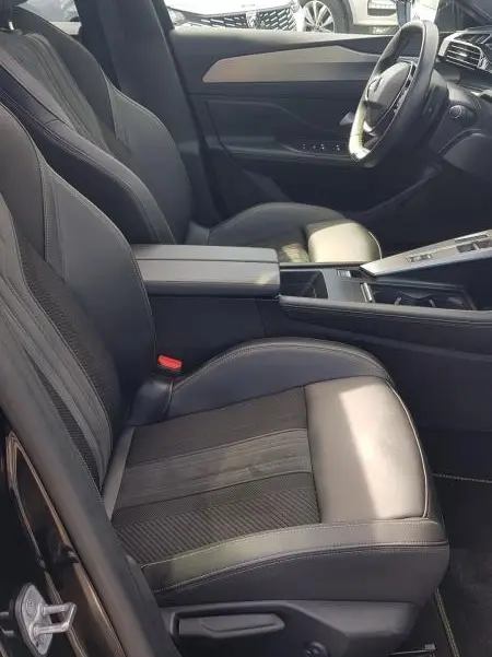 Intérieur avant droit de la Peugeot 308 SW PHEV 225 GT 2023 noire, sièges cuir avec accoudoir central et volant cuir.