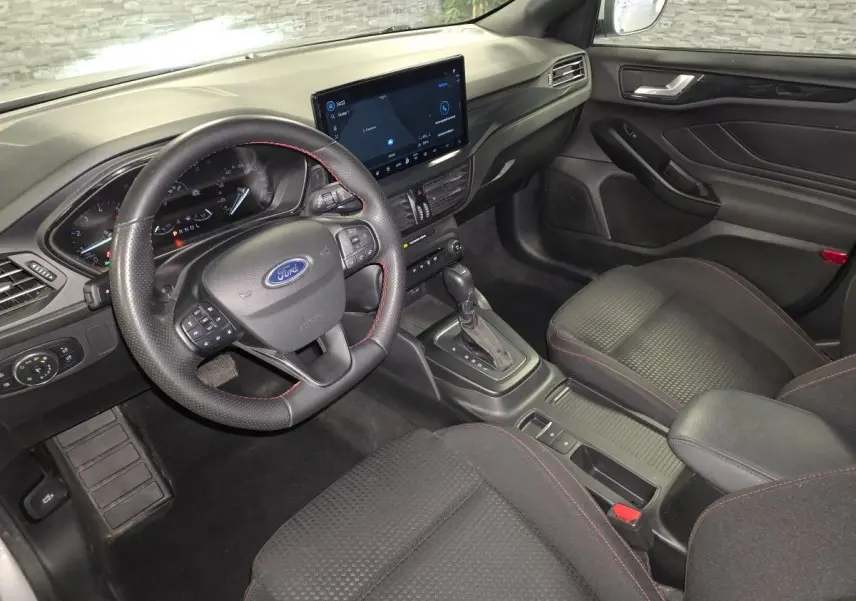 Vue intérieure côté conducteur de la Ford Focus 2024 gris, volant ST à surpiqûres rouges et écran tactile central.