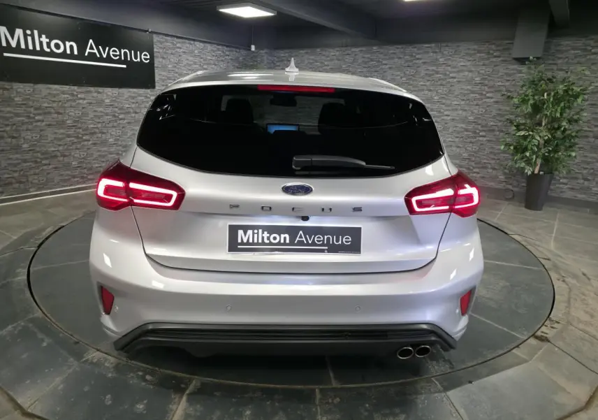 Vue arrière d'une Ford Focus gris lunaire 2024 avec feux LED allumés et double sortie d'échappement sport.