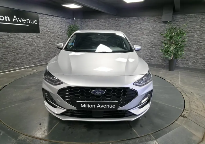 Vue avant d'une Ford Focus gris métallisé avec calandre noire et badge ST-Line visible en intérieur showroom.