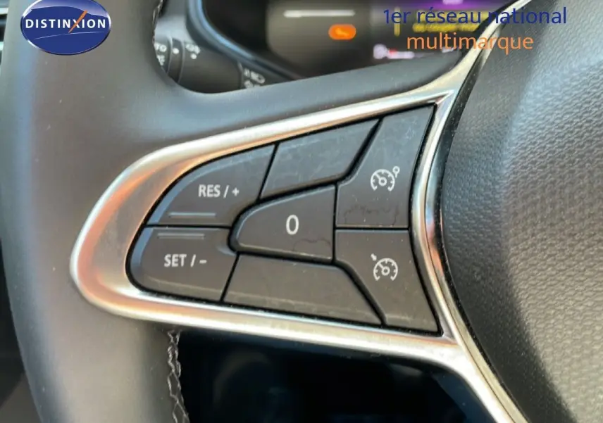 Gros plan sur les commandes de régulateur de vitesse au volant noir de la Renault Clio blanc glacier 2025.