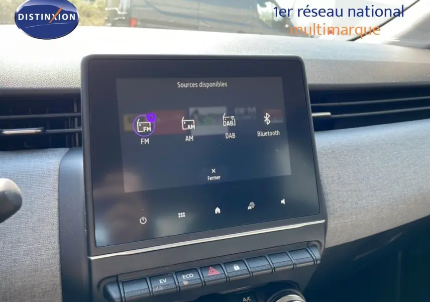 Vue intérieure centrée sur l'écran tactile multimédia de la Renault Clio blanche Glacier, avec commandes climatisation et mode EV visibles.