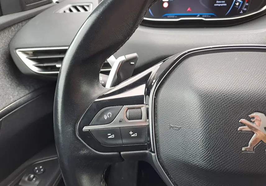 Gros plan sur le volant noir du Peugeot 3008 blanc 2018, avec commandes intégrées et tableau de bord partiellement visible.