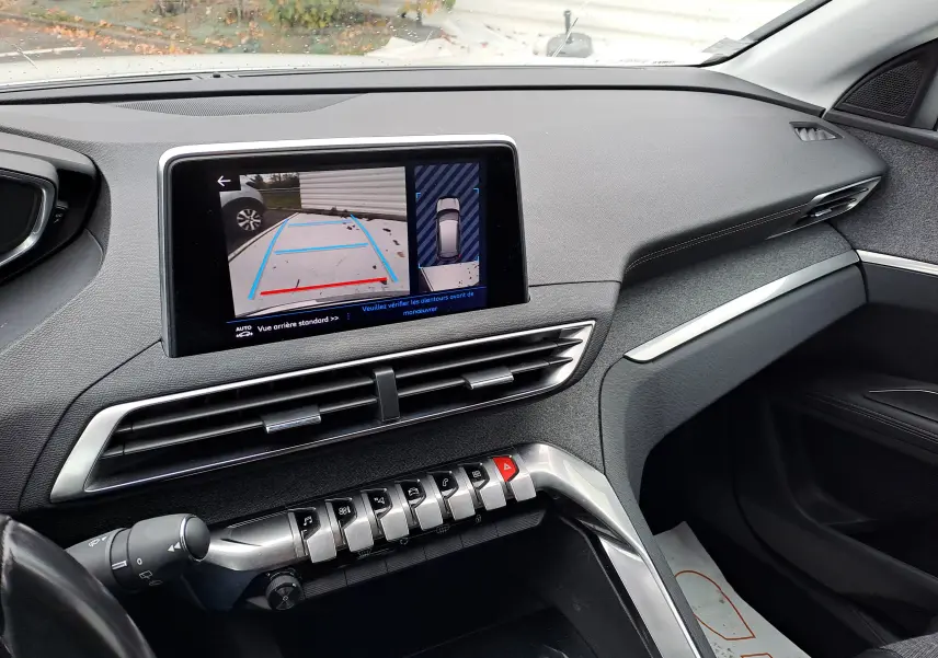 Tableau de bord intérieur du Peugeot 3008 blanc, avec écran affichant la caméra de recul et commandes centrales modernes.