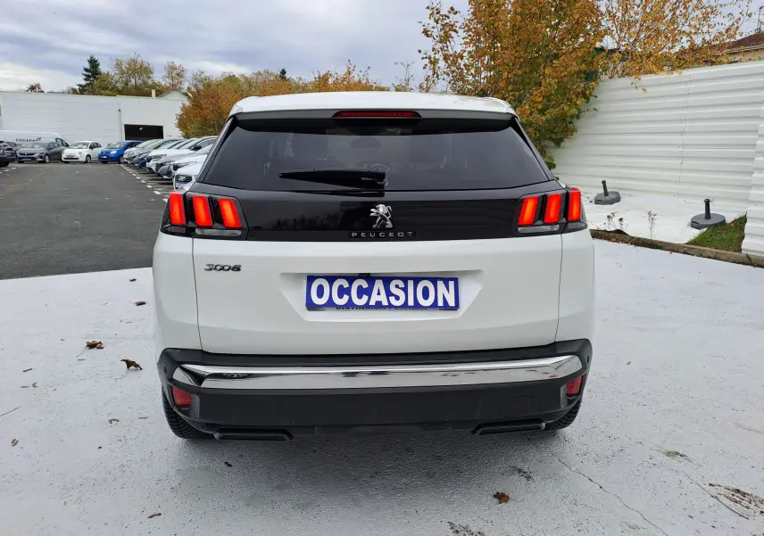 Vue arrière d'un Peugeot 3008 blanc avec feux arrière allumés et plaque "OCCASION" sur un parking extérieur.
