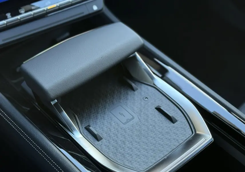 Gros plan sur le chargeur sans fil noir et accoudoir central du Renault Espace VI hybride 2025.